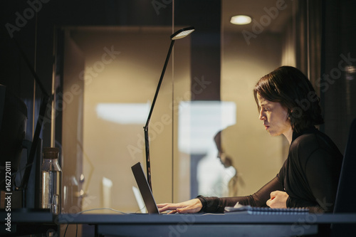 Side view of businesswoman using laptop at desk in dark office