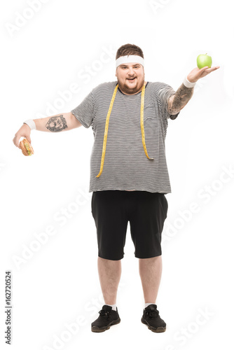 smiling fat man holding burger and apple isolated on white © LIGHTFIELD STUDIOS