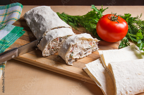 Pieces of cutted pita bread or lavash roll with cottage cheese or curd, chicken, tomatoes and herbs - dill, onion, parsley with intige knife on cutting board.. photo