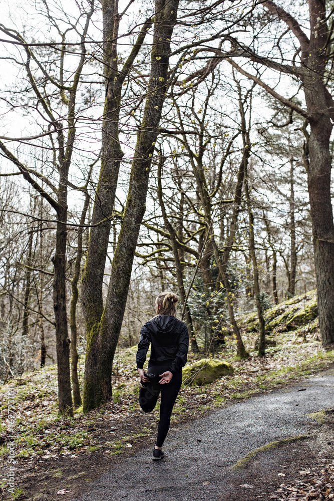 Full length rear view of female athlete doing stretching exercise on road in forest Full length rear view of female athlete doing stretching exercise on road in forest
