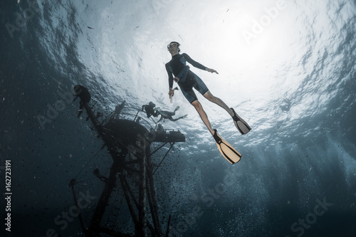 Woman freediver dives deep underwater along the ship wreck