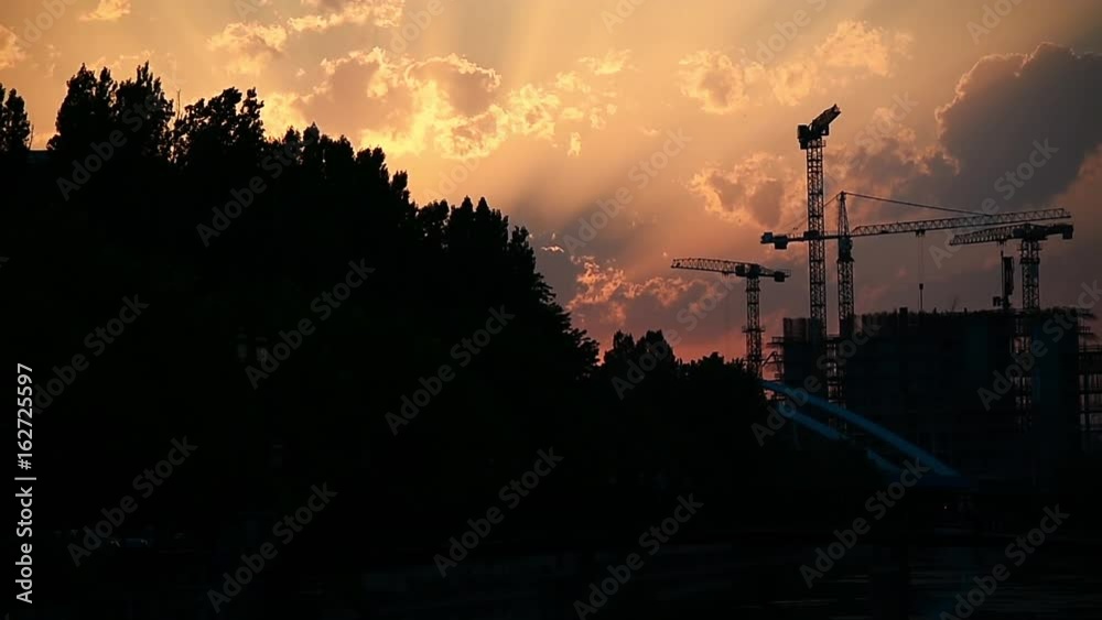 Construction cranes silhouetted against sunset sky Construction cranes silhouetted against sunset sky