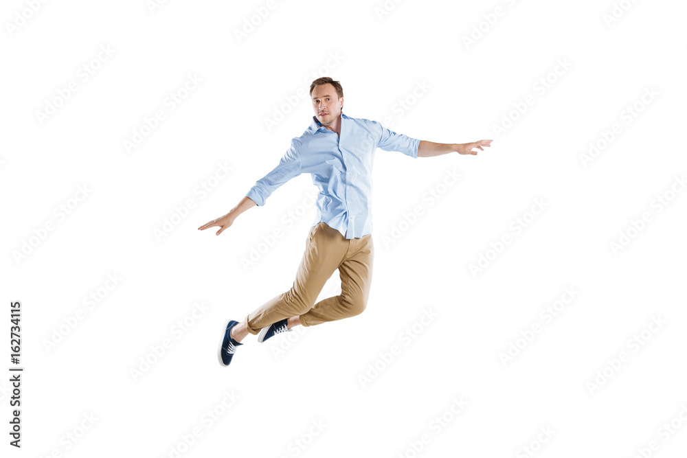young casual man jumping with arms outstretched isolated on white