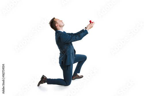 young man in suit standing on one knee and making marriage proposal isolated on white photo