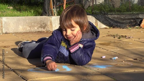 4K Cute kid lazily draws with chacks lying on concrete slabs photo