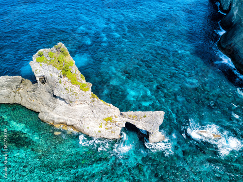 Dramatic aerial view of the coral reef surrounding the natural arch near Atuh Beach on Nusa Penida, Bali, Indonesia.
