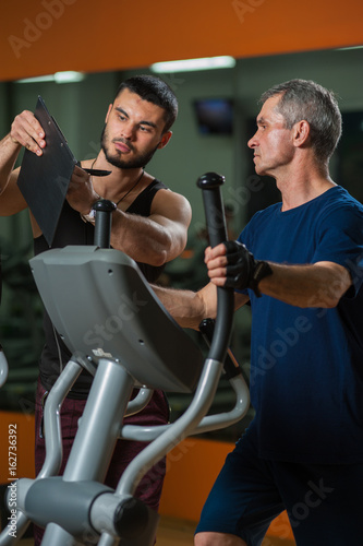 Senior man working in gym with personal trainer