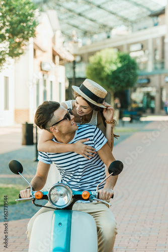 Happy stylish young couple sitting on scooter and hugging