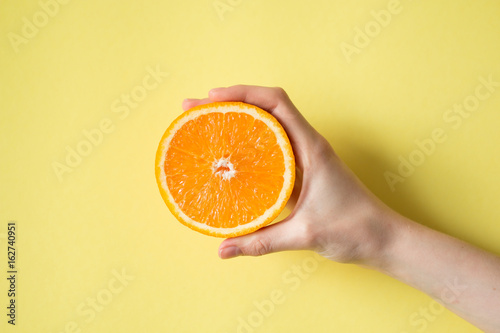 Hand holding orange on yellow background food concept