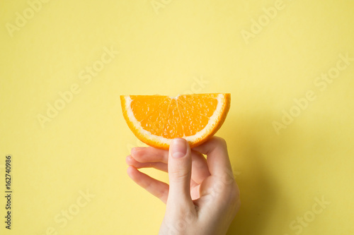 Hand holding orange on yellow background food concept