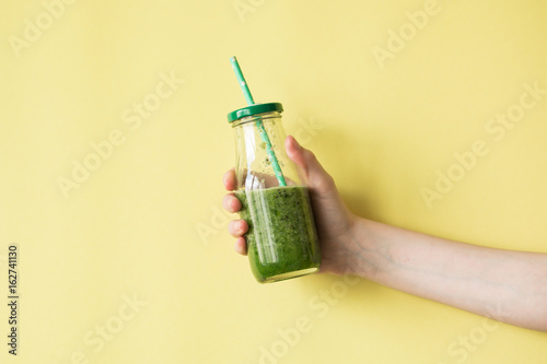 Woman hand holding smoothie shake against colored wall. Drinking green healthy smoothie concept.