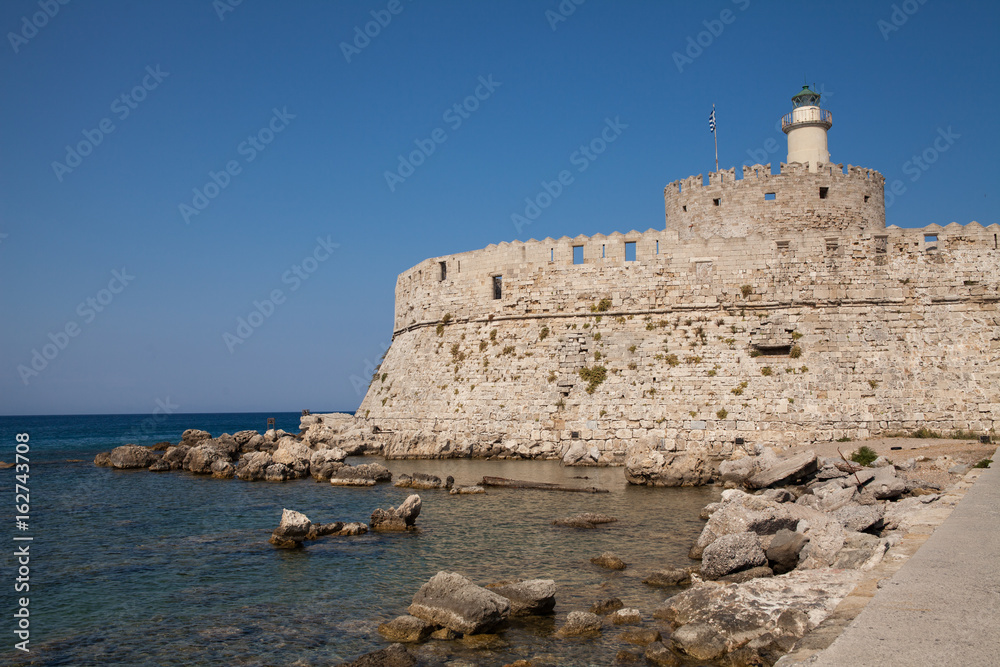 Santa Claus Fortress on the pier in Mandraki Harbor. Bastion of defense on the quay of Rhodes. A defensive building in a harbor in the town of Rhodes with a lighthouse.