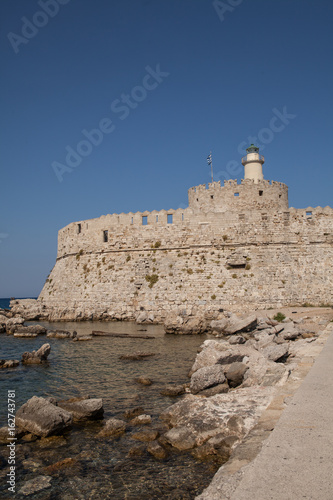 Santa Claus Fortress on the pier in Mandraki Harbor. Bastion of defense on the quay of Rhodes. A defensive building in a harbor in the town of Rhodes with a lighthouse.