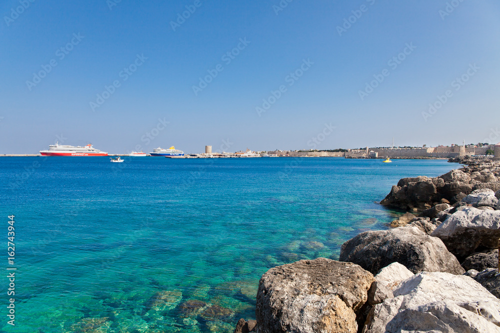 View of the sea and harbor fragment of Rhodes. Stones in the blue lagoon and passenger ships.