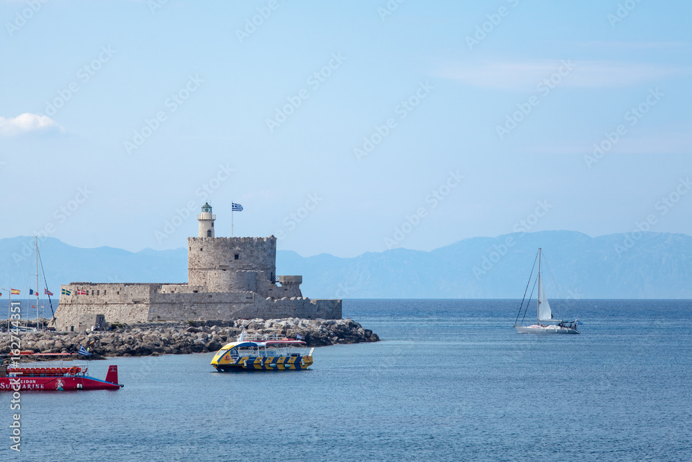 Santa Claus Fortress on the pier in Mandraki Harbor. Bastion of defense on the quay of Rhodes. Harbor and monuments in Rhodes. Old defensive walls and windmills.
