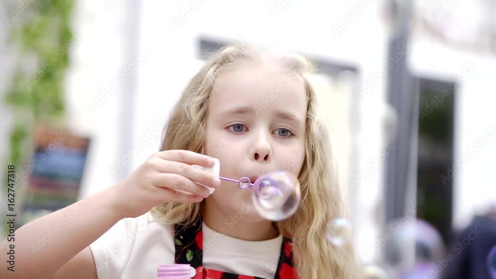 Cute little girl is blowing soap bubbles in the garden outdoors on a sunny day. Happy childhood concept. Child is playing in bright sun light. Cute little girl is blowing soap bubbles in the garden outdoors on a sunny day. Happy childhood concept. Child is playing in bright sun light.