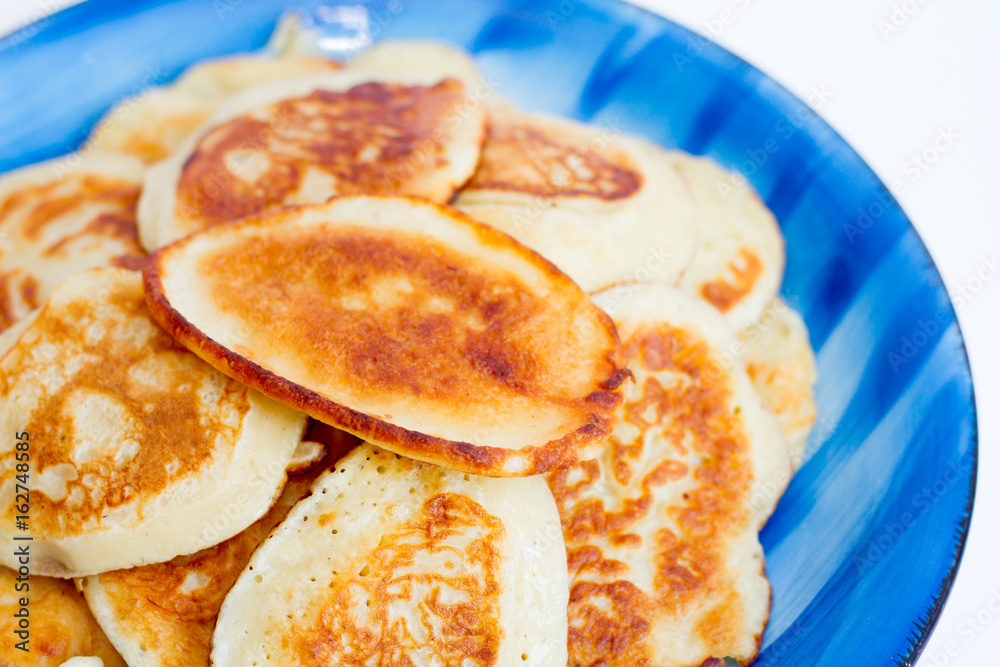 Ruddy freshly cooked pancakes lie on a blue plate on a white background. Ruddy freshly cooked pancakes lie on a blue plate on a white background.