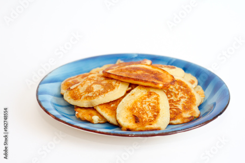 Ruddy freshly cooked pancakes lie on a blue plate on a white background.