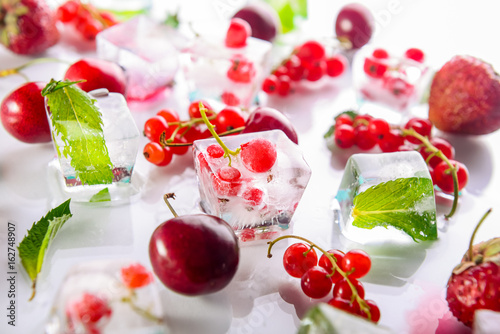 Photos Close up ice cubes with fresh berries among not frozen cherry, strawberry and mint leafs on the white background