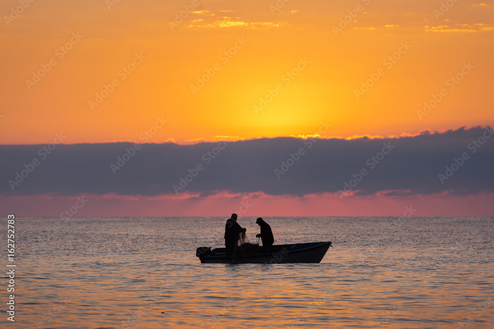 Two fishermen on a boat fishing on a sea with beautiful sunrise in background