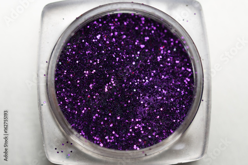 Closeup of purple nail makeup glitter in round jar isolated on silver background. Concept of beauty and makeup