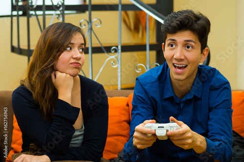 Handsome young man playing video games on the couch while girlfriend is bored, concept about home entertainment, video games photo