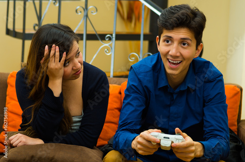 Handsome young man playing video games on the couch while girlfriend is bored, concept about home entertainment, video games photo