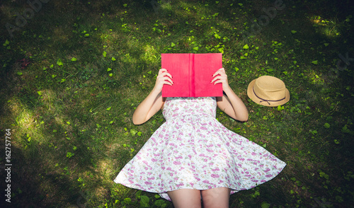 Woman reading a book and covering face outside on the grass