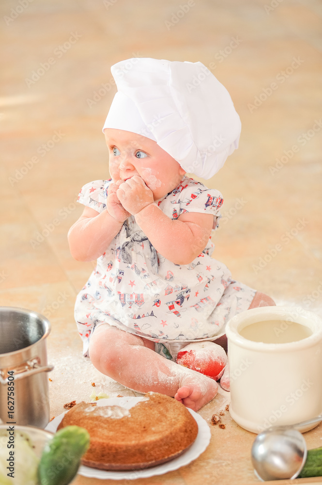 Cute liitle girl in chef's hat sitting on the kitchen floor soiled with flour, playing with food, making mess and having fun Cute liitle girl in chef's hat sitting on the kitchen floor soiled with flour, playing with food, making mess and having fun