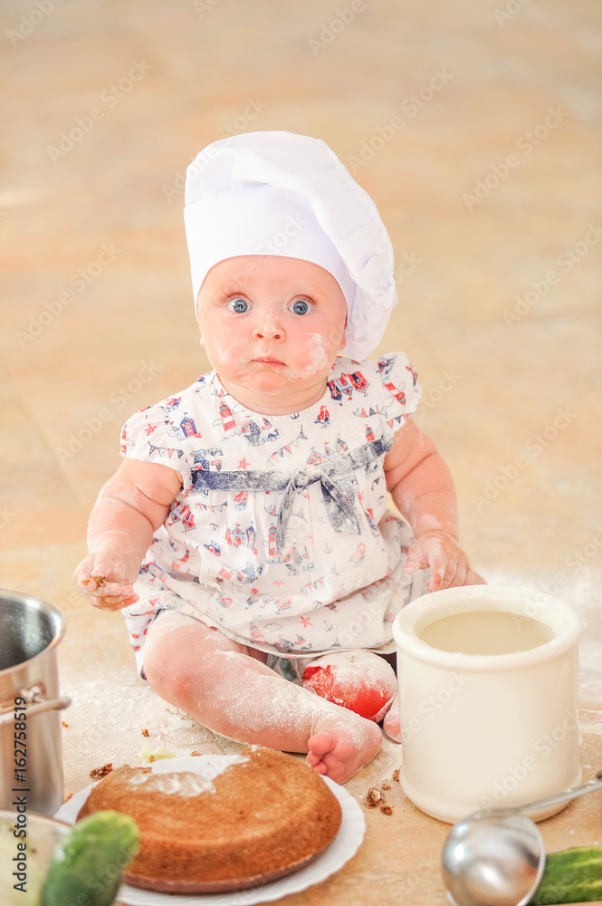 Cute liitle girl in chef's hat sitting on the kitchen floor soiled with flour, playing with food, making mess and having fun Cute liitle girl in chef's hat sitting on the kitchen floor soiled with flour, playing with food, making mess and having fun