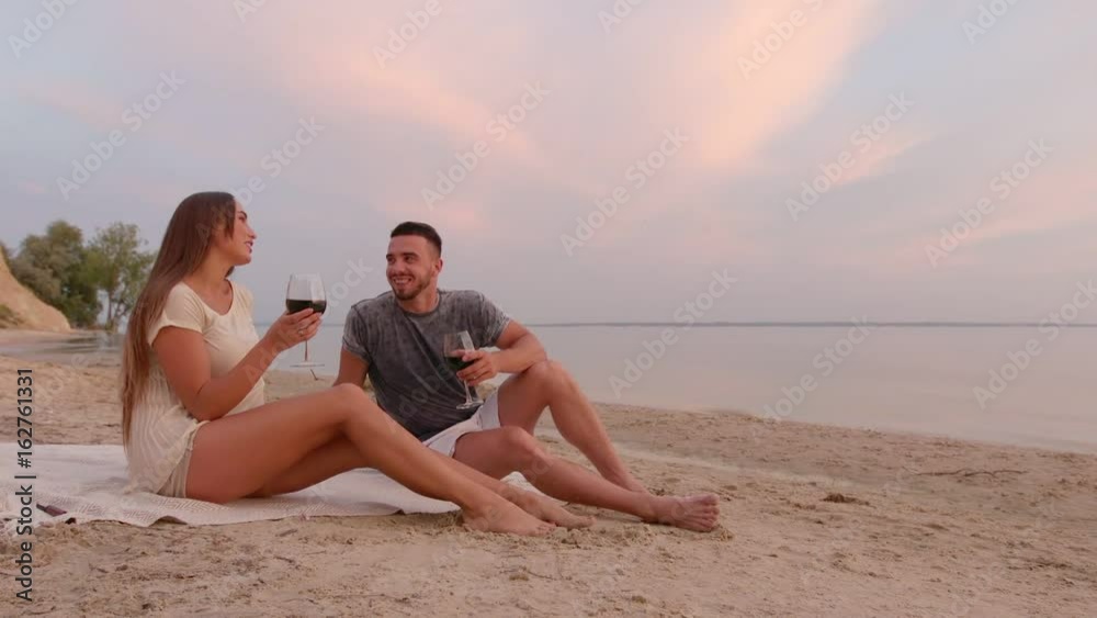 Young beautiful brunette couple in love on romantic date at beach at sunset drinking wine Young beautiful brunette couple in love on romantic date at beach at sunset drinking wine