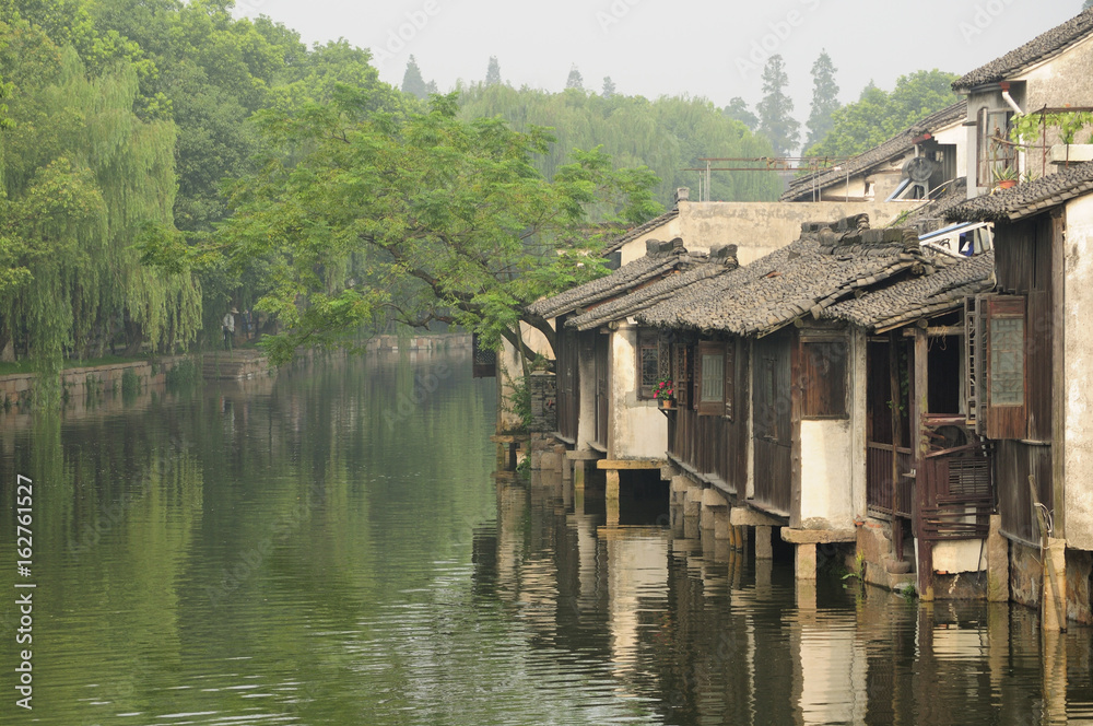 Wooden, weathered buildings lining the water canals in tongxiang wuzhen scenic town east view in Zhejiang province China in the early morning mist.