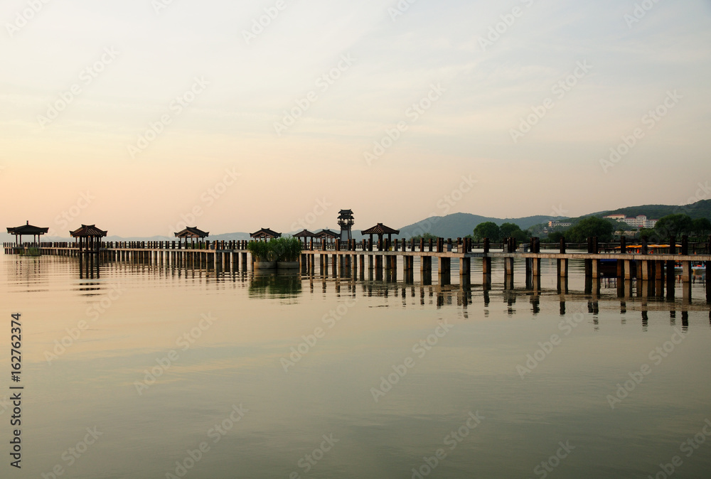 A long pier and asian covered gazebos and tower over the water of Tai Lake at the Three Kingdoms Scenic area.