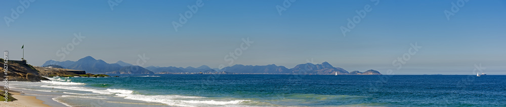 Panoramic view of Devil's beach and the Copacabana fort with brazilian flag and the hills of the city of Niteroi in the background