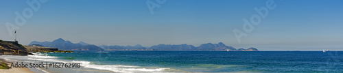 Panoramic view of Devil's beach and the Copacabana fort with brazilian flag and the hills of the city of Niteroi in the background