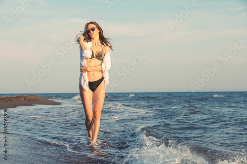 Fototapeta Naklejka Na Ścianę i Meble -  Attractive young woman walking along sea or ocean beach at sunset