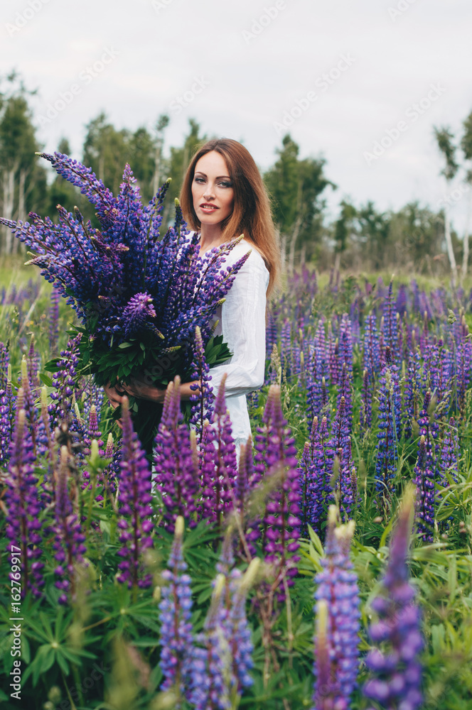 A girl in a white dress is standing among the lupines A girl in a white dress is standing among the lupines