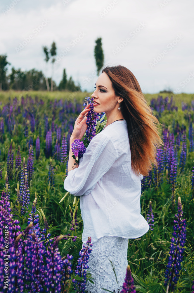 A girl in a white dress is standing among the lupines A girl in a white dress is standing among the lupines