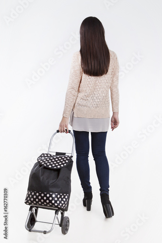 Woman keeps bag with wheels for shopping isolated on white background. Back view