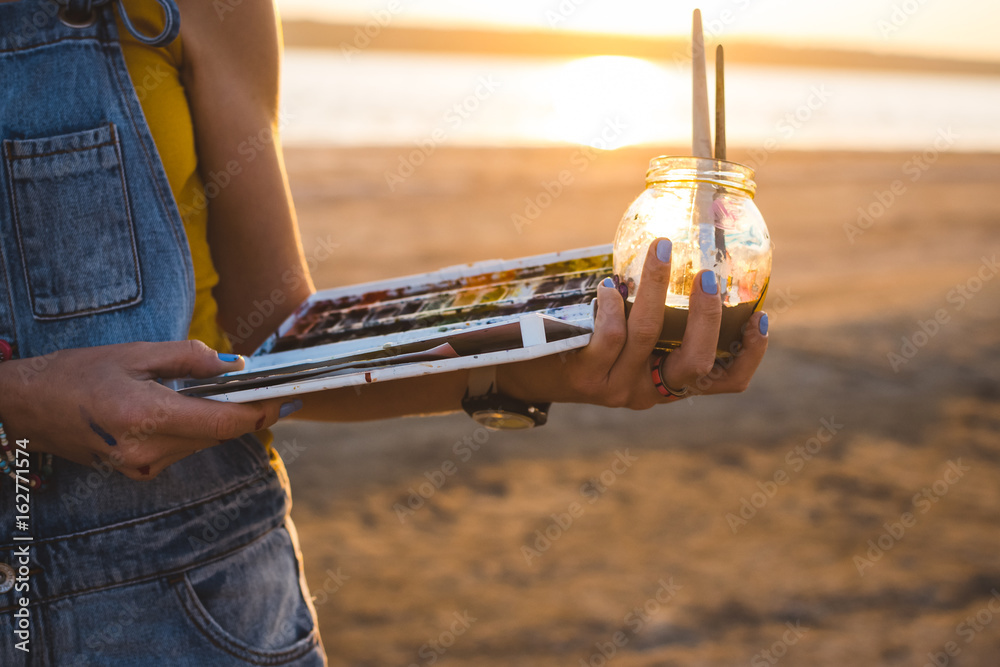 Fototapeta premium Young woman artist painting landscape in the open air on the beach, close up