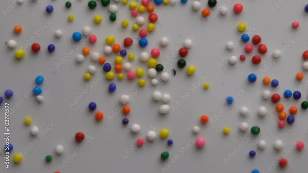Colorful sprinkles sugar candy moving on white surface background Colorful sprinkles sugar candy moving on white surface background