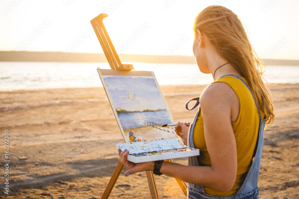 Obraz premium Young woman artist painting landscape in the open air on the beach