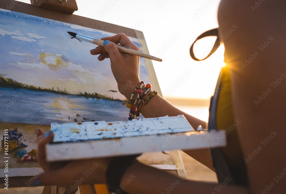 Naklejka premium Young woman artist painting landscape in the open air on the beach, close up