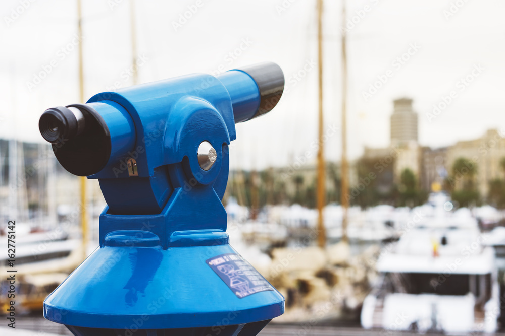 Touristic telescope look at the city with view of Barcelona Spain, close up old blue binoculars on background viewpoint  the pier port yacht, coin operated  in panorama observation nature, mockup