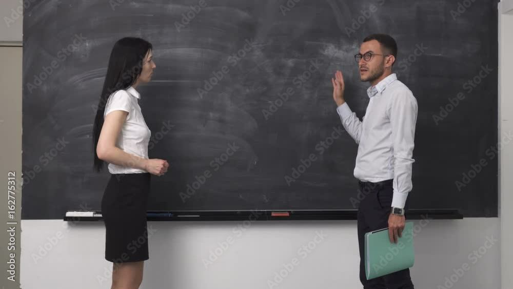 Business meeting young man is explaining something near the blackboard to a woman Business meeting young man is explaining something near the blackboard to a woman