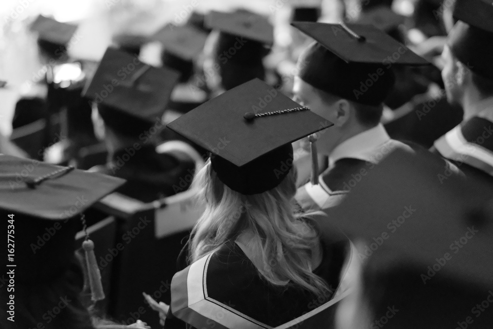 Square academic caps of graduates sitting in the university hall at the presentation of diplomas. Square academic caps of graduates sitting in the university hall at the presentation of diplomas.
