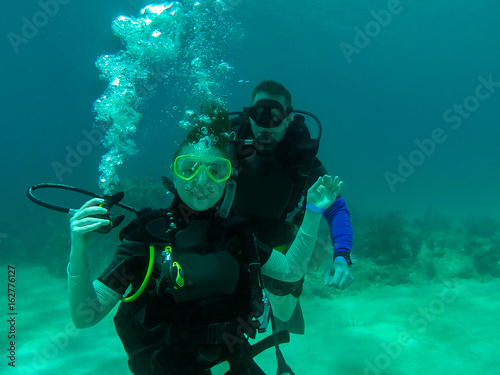 A couple scuba dive together. A female scuba diver with the regulator out. Smiling, holding the regulator. Divers. Roatan, Honduras