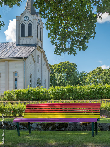 Canvas Print Rainbow flag colors on bench, church in background