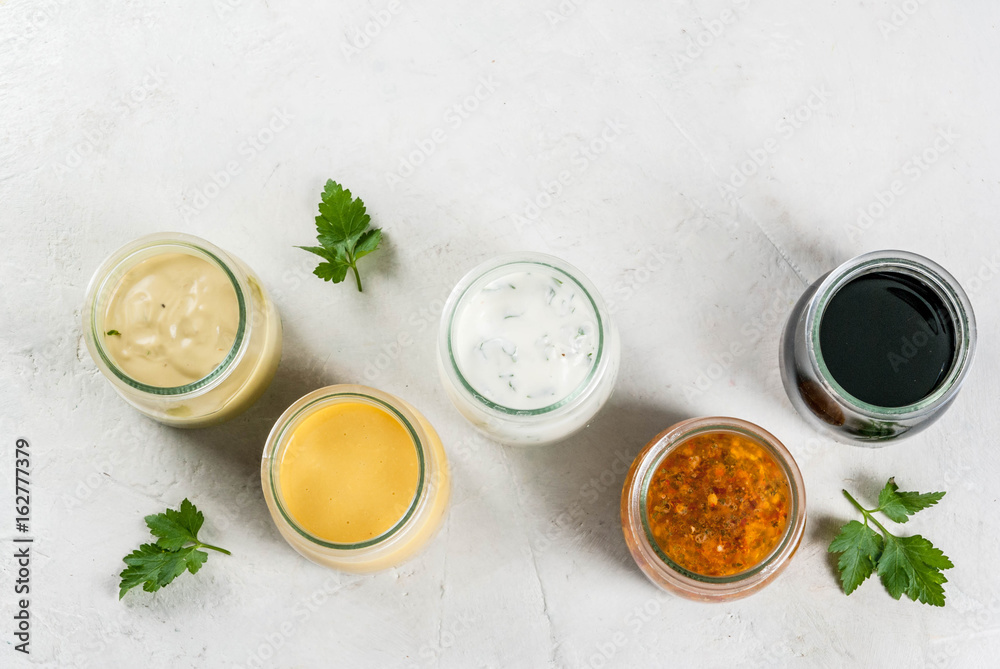 Set of dressings for salad: sauce vinaigrette, mustard, mayonnaise or ranch, balsamic or soy, basil with yogurt. Dark white concrete table. Copy space top view Set of dressings for salad: sauce vinaigrette, mustard, mayonnaise or ranch, balsamic or soy, basil with yogurt. Dark white concrete table. Copy space top view