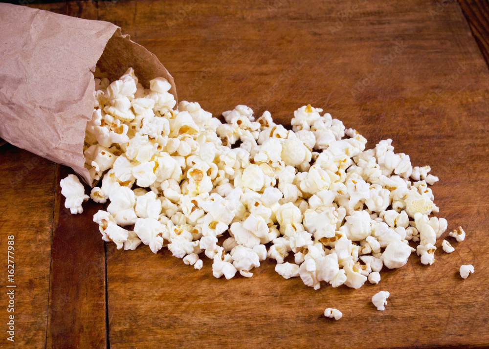 White fluffy salty popcorn in package on wooden table White fluffy salty popcorn in package on wooden table